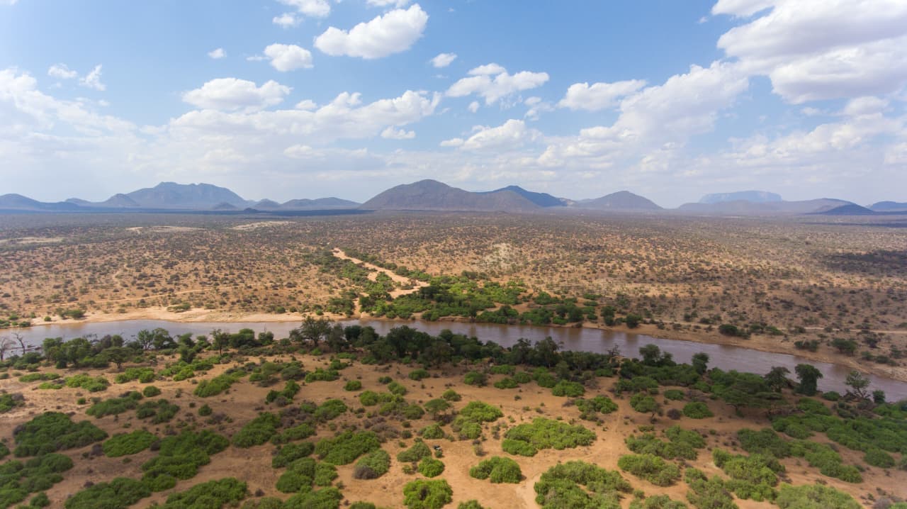 High aerial view of the Ewaso Ny'iro River crossing vast ASAL plains dotted with scattered green bush