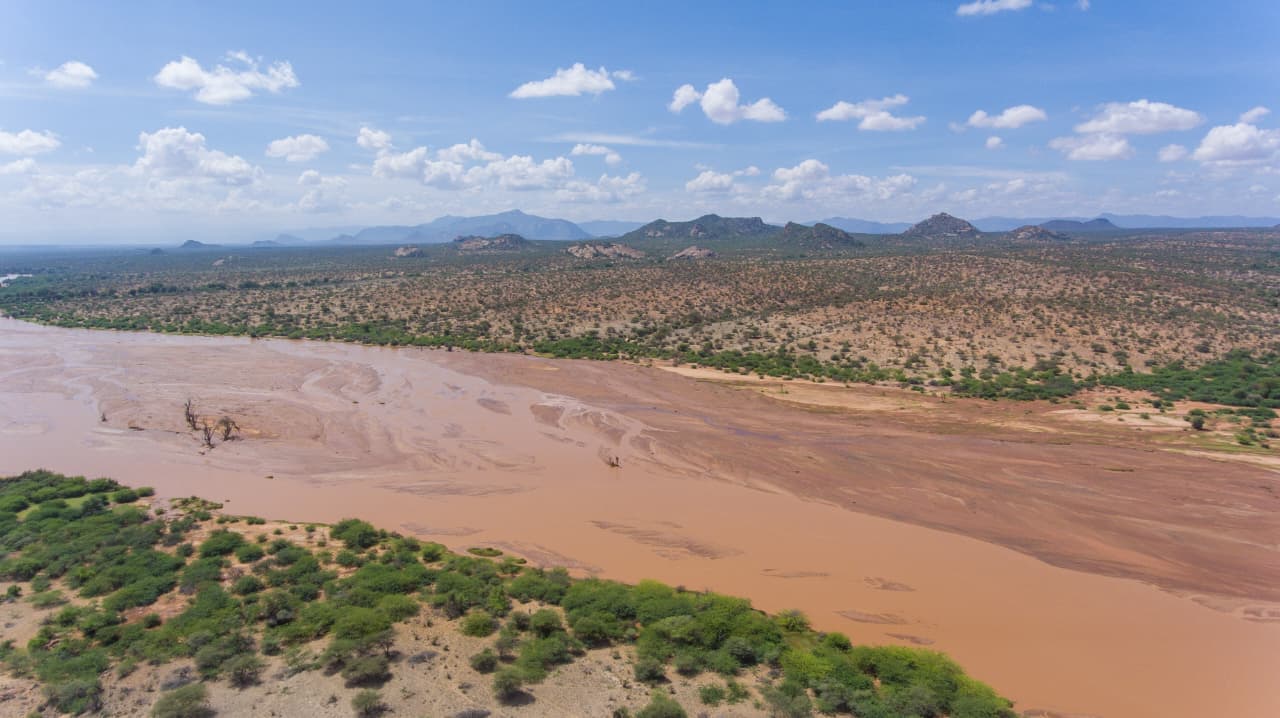 Aerial view of the wide muddy flood plain of the Ewaso Ny'iro River with rocky hills beyond