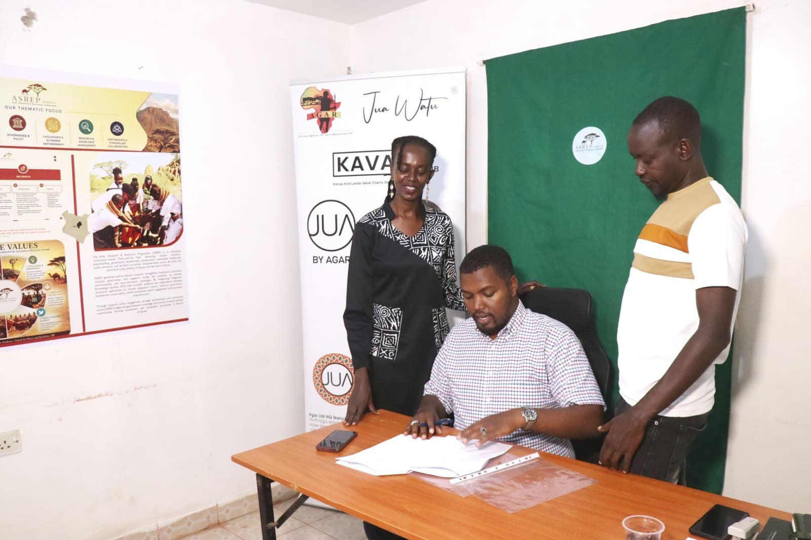 Partners looking on as Dida Fayo reviews the MOU pages before signing at the ASREP–AGAR ceremony