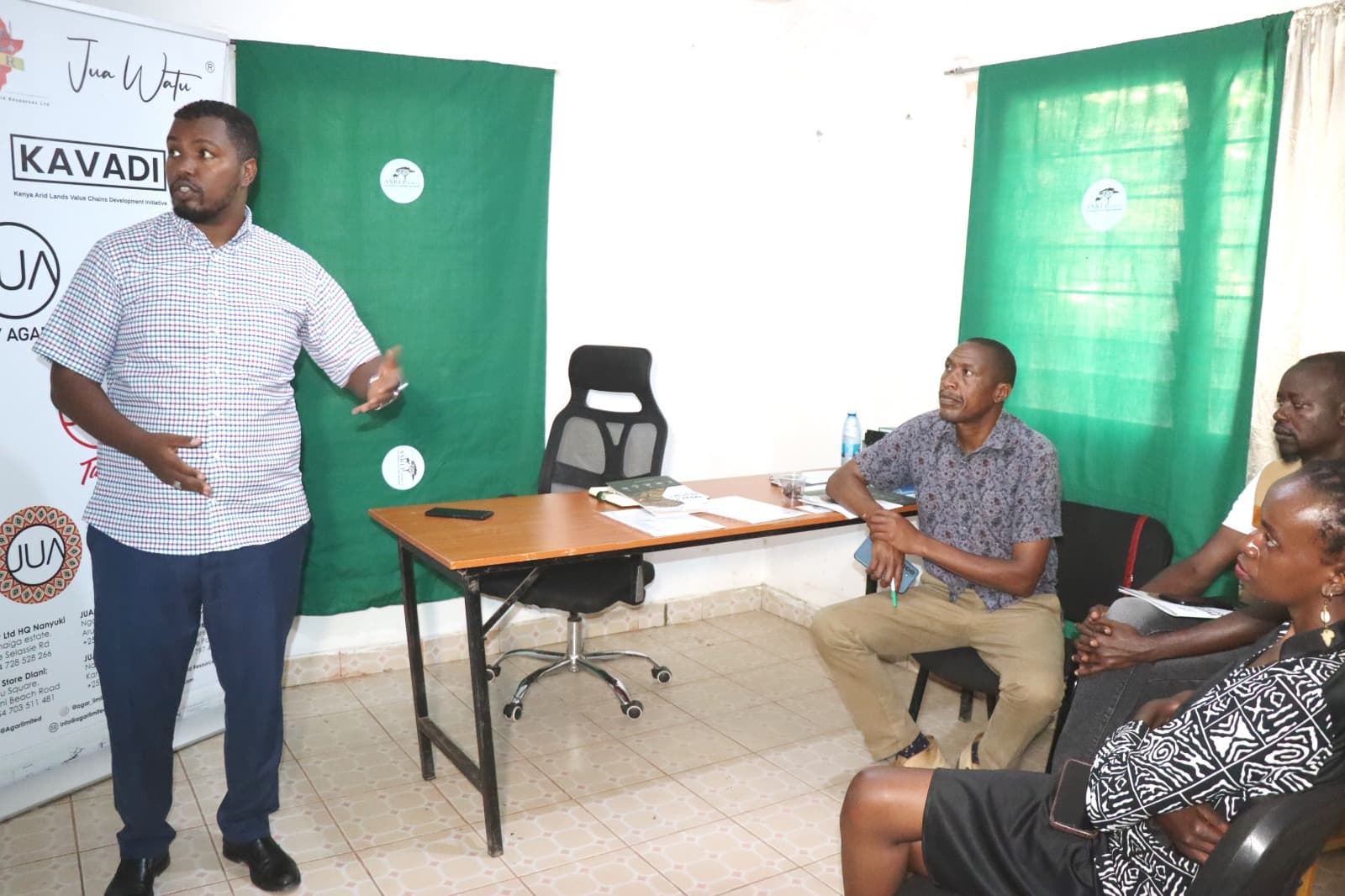 Dida Fayo standing and presenting to the seated AGAR delegation at the ASREP office, KAVADI Hub banner at left