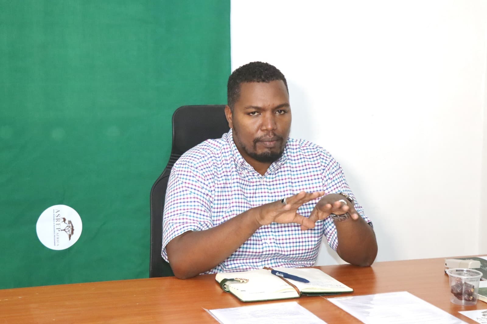 ASREP Africa Executive Director Dida Fayo giving remarks at the desk during the AGAR MOU signing, green ASREP backdrop with logo