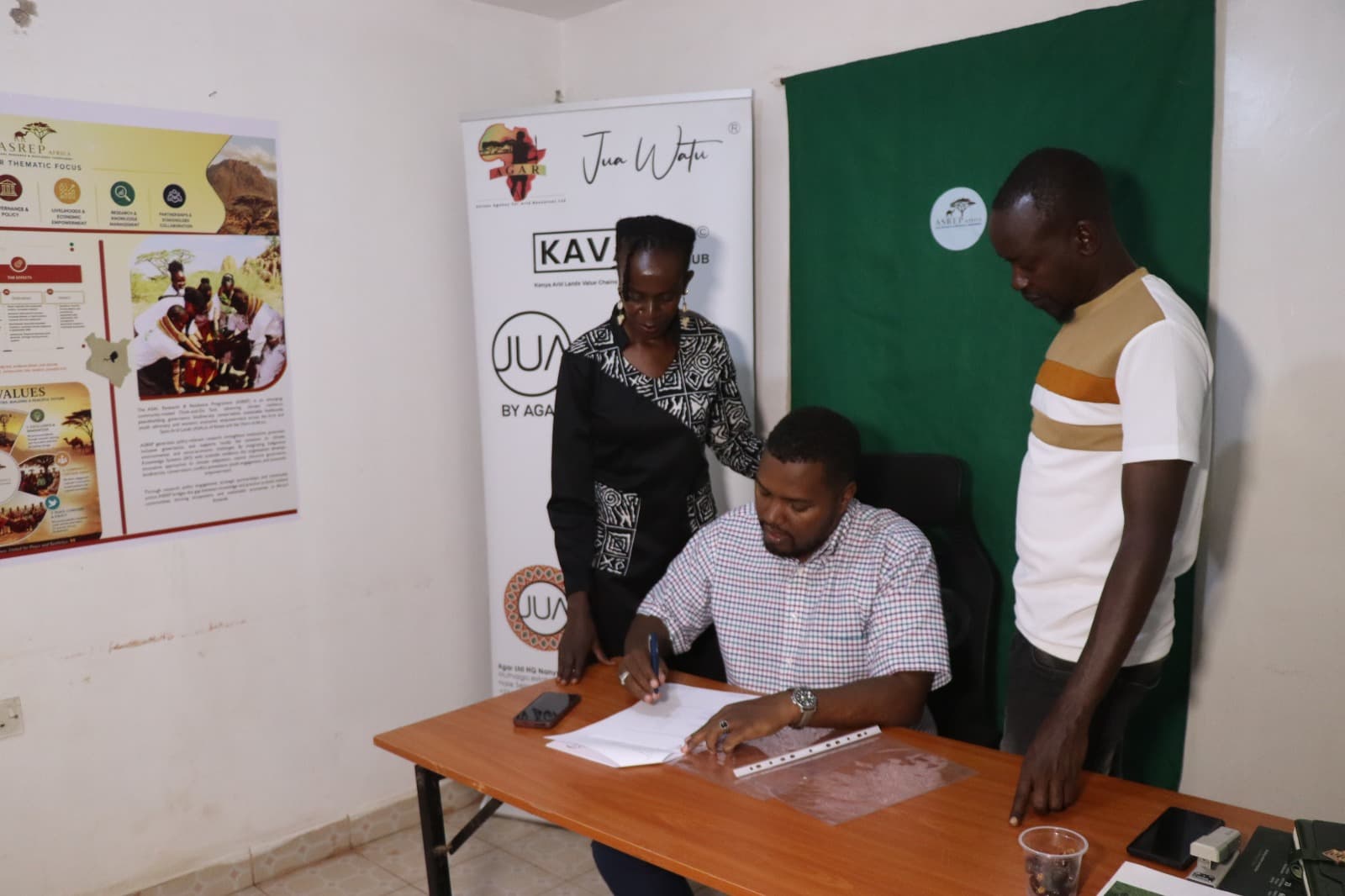 Dida Fayo signing the MOU Framework Agreement at the desk with the AGAR representative and a colleague standing by