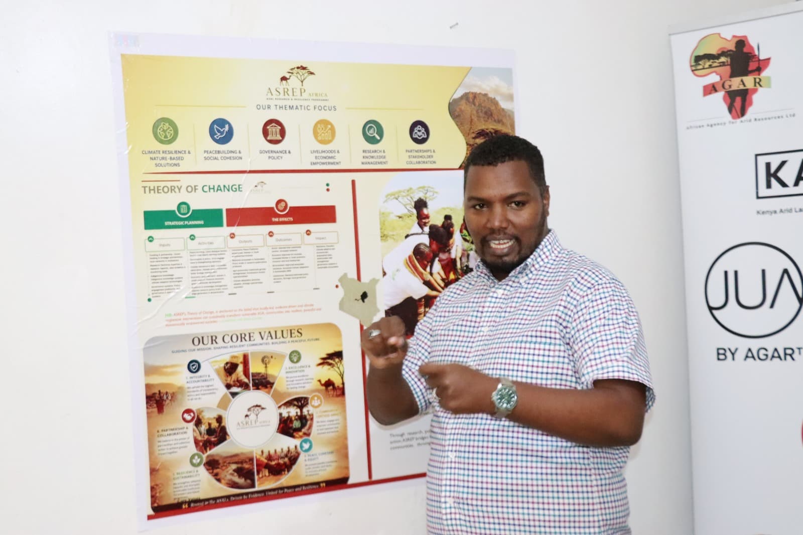 Dida Fayo pointing at Kenya on the ASREP Our Thematic Focus and Theory of Change poster, AGAR banner beside him